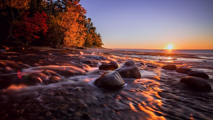 Sunset over a rocky shore with autumn trees