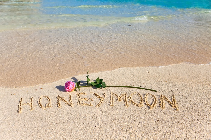 Honeymoon written in sand with a rose on a beach