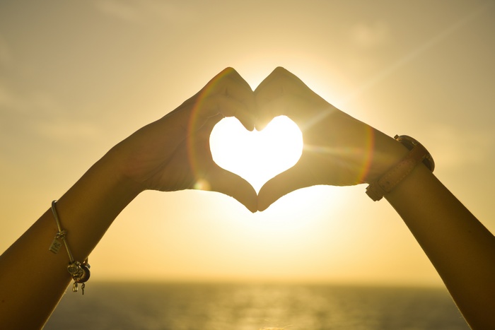 Hands forming a heart shape at sunset