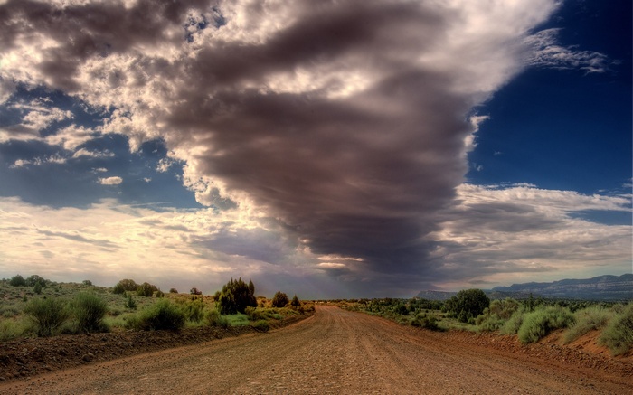 Dirt road through a desert landscape under dramatic clouds
