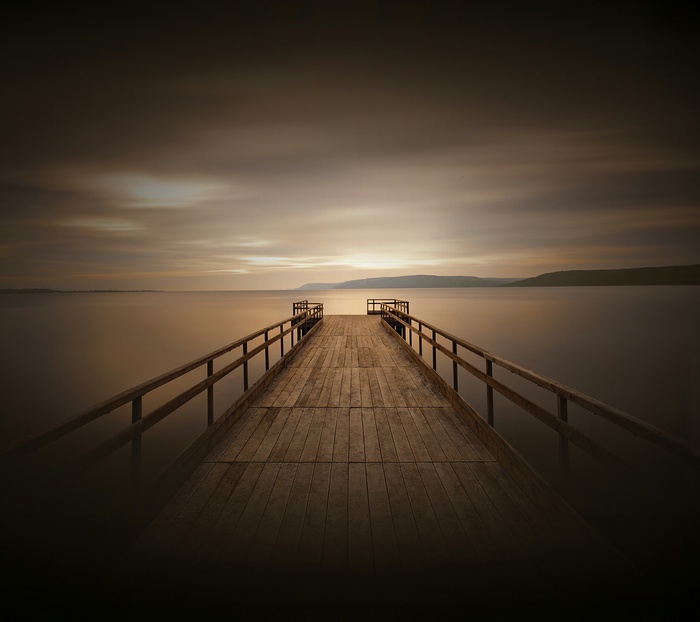 Wooden dock extending into a calm sea at sunset