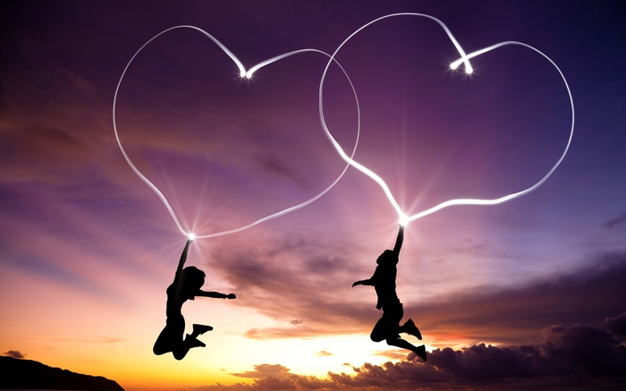 Couple drawing hearts in the sky at sunset
