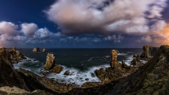 Rocky coastline at night with crashing waves and clouds