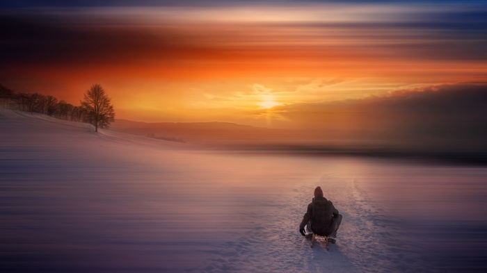 Person sledding in snow at sunrise