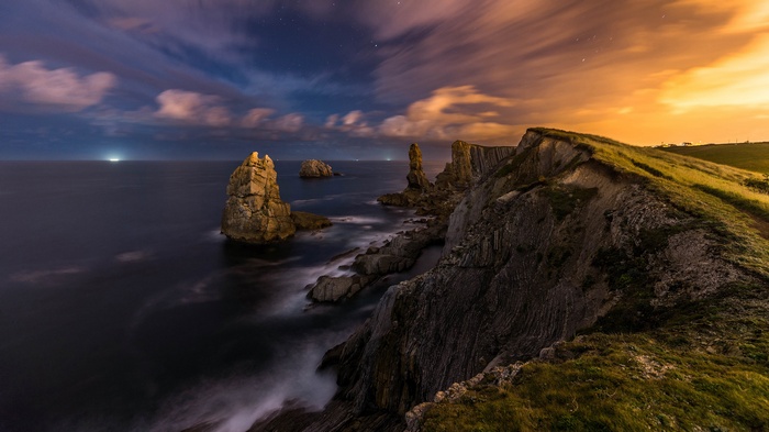 Rocky coastline at night with dramatic clouds and ocean waves