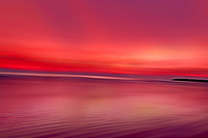 Crimson sunset over a calm ocean with a distant island