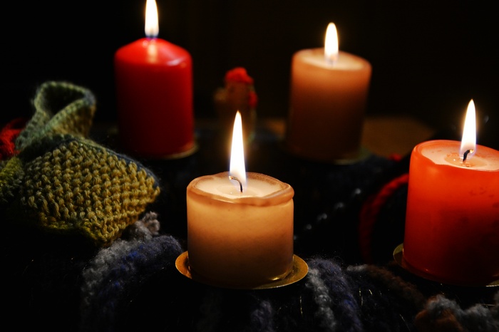 Four lit candles on a dark background with knitted items