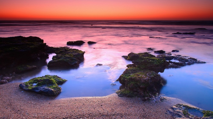 Sunset over rocky ocean shore with pink and orange sky