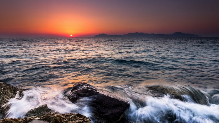 Sunset over the ocean with waves crashing on rocks