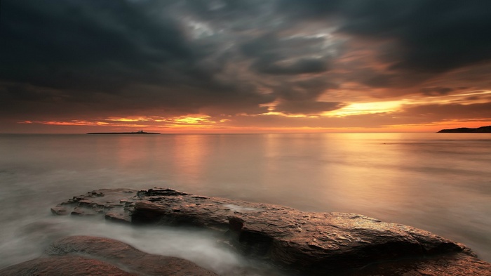 Sunset over the ocean with a lighthouse on an island