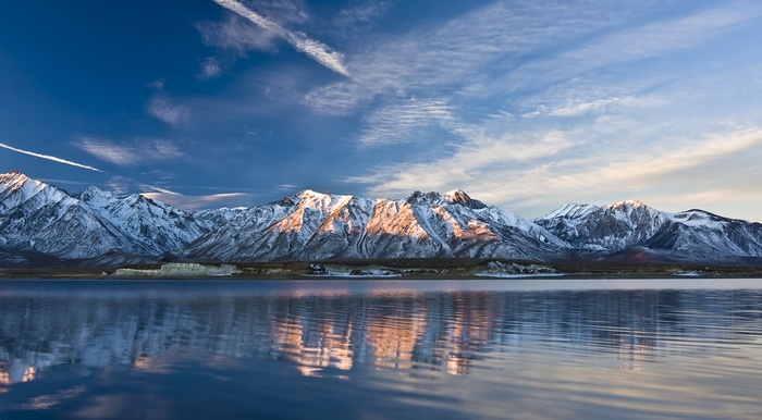Snow-capped mountains reflected in a lake under a blue sky