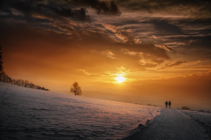 Couple walking on snowy path during sunset