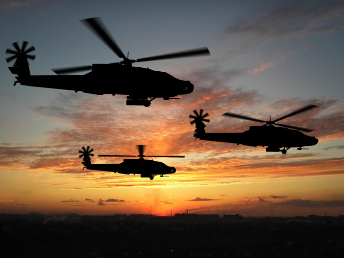 Three Apache helicopters flying at sunset over a city
