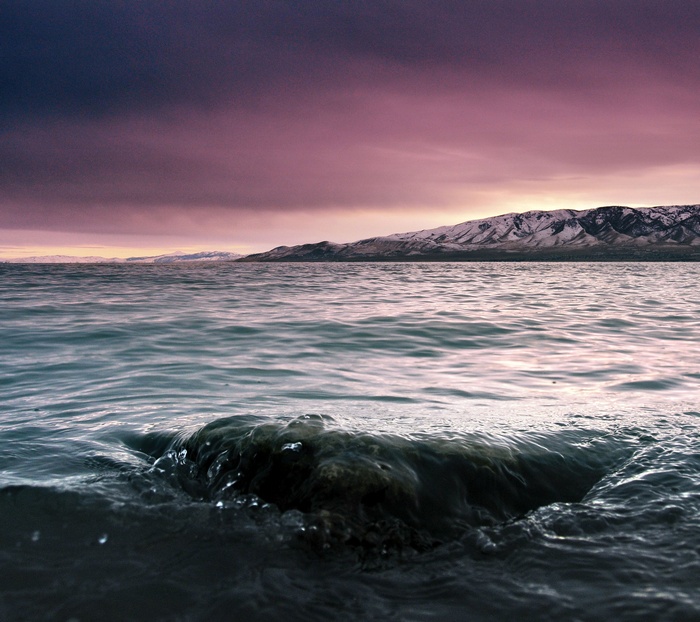 Rock in water with purple sky and snowy mountains