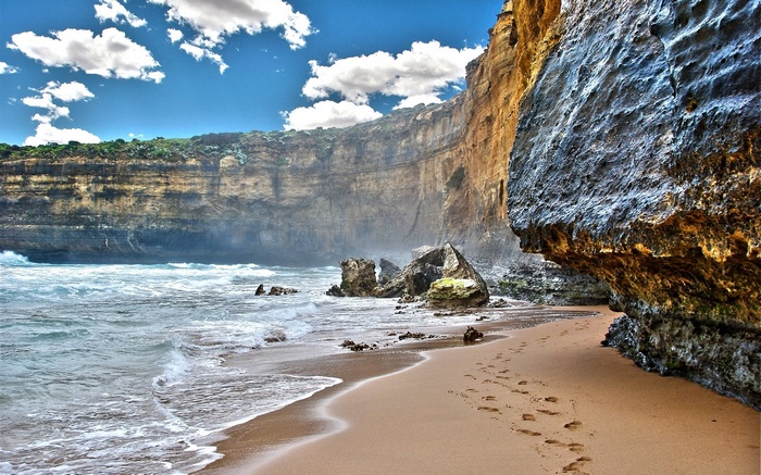 Footprints on a sandy beach with cliffs and ocean waves