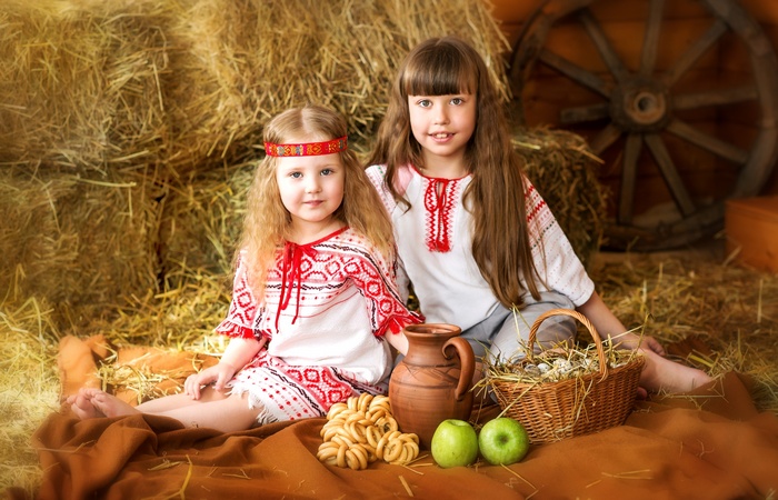 Two young girls in traditional clothing sitting in hay
