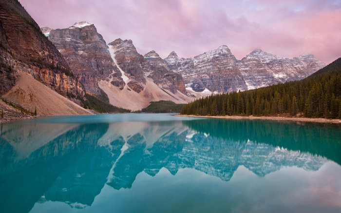 Turquoise lake reflecting snow-capped mountains and pine forest