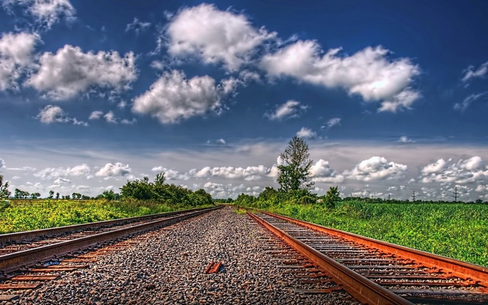 Train tracks through a green field under a cloudy sky