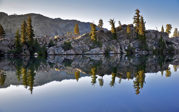 Lake reflection of rocky shore with pine trees