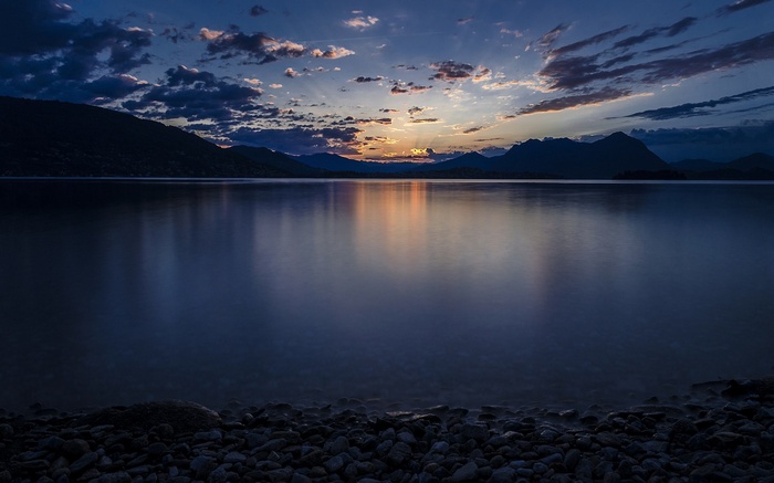 Sunset over a calm lake with mountains and clouds