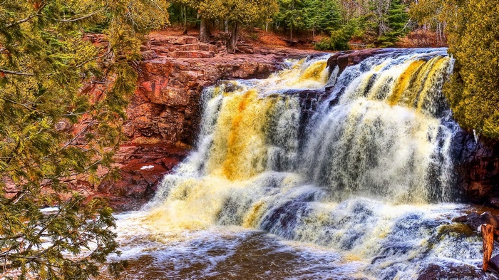 Waterfall cascading over red rocks with autumn trees