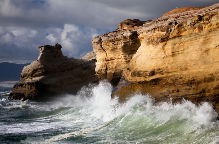 Waves crashing against rocky cliffs under a cloudy sky