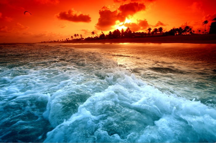 Sunset over a beach with waves and a kite surfer