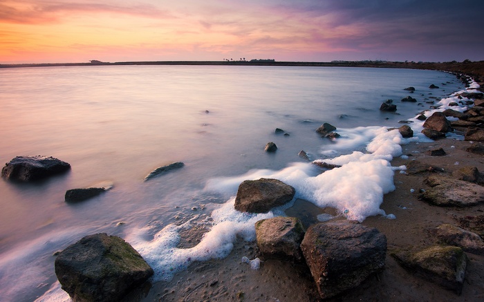 Ocean waves with foam washing over rocks at sunset