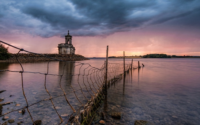 Church on a rocky island at sunset with a fence