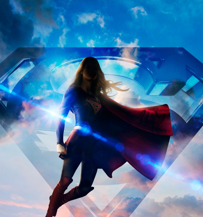 Supergirl flying in front of a large S shield