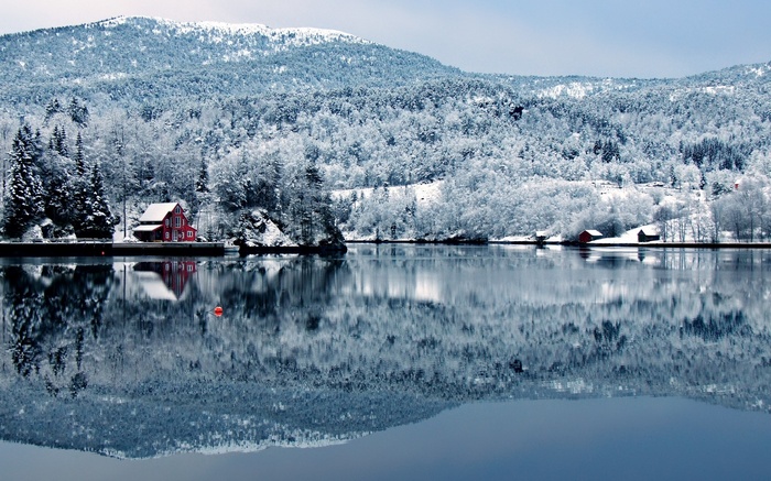 Red house on a snowy lake with mountains