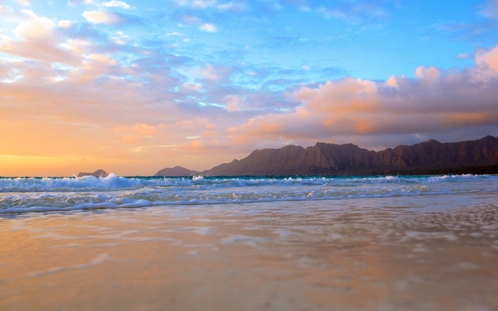Beach with mountains and ocean waves at sunset