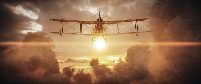 Biplane flying through clouds at sunset