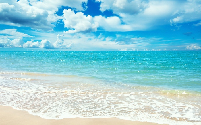 Turquoise ocean waves on a sandy beach under a cloudy blue sky