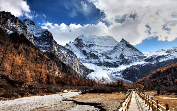 Wooden bridge leading to snow-capped mountains in autumn