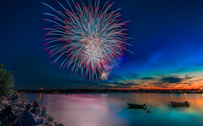 Fireworks over a lake at dusk with people watching