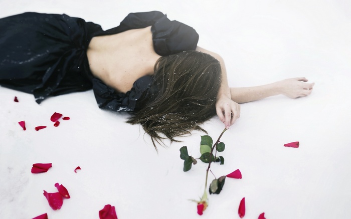 Woman in black dress lying in snow with rose petals