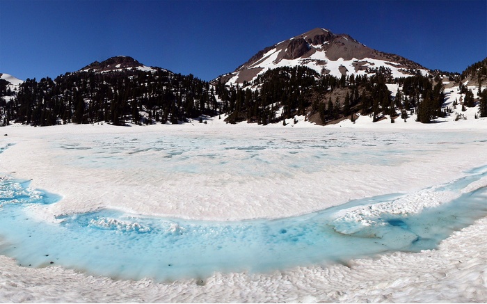 Frozen lake with mountains and pine trees