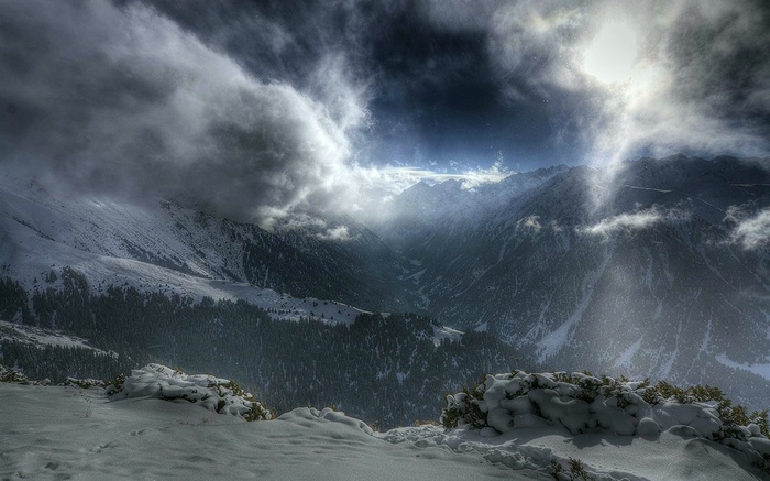 Snowy mountain valley with dramatic clouds and sunbeams