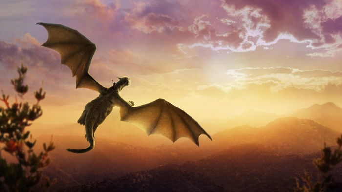 Dragon with rider flying over mountains at sunset