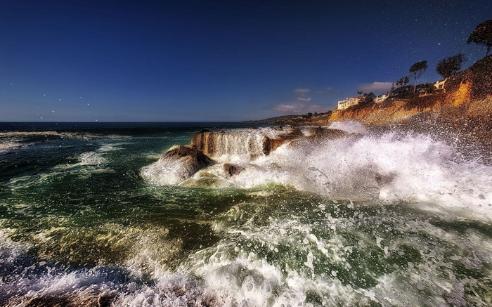 Waves crashing on rocky shore with houses on cliff
