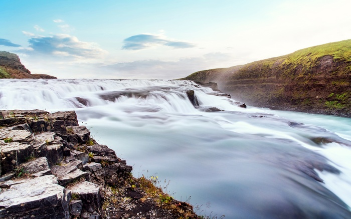 Wide waterfall cascading over rocks under a blue sky