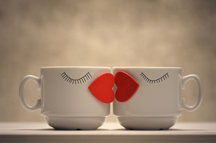 Two coffee mugs kissing with hearts