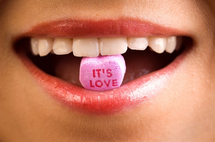 Close-up of lips holding a candy heart