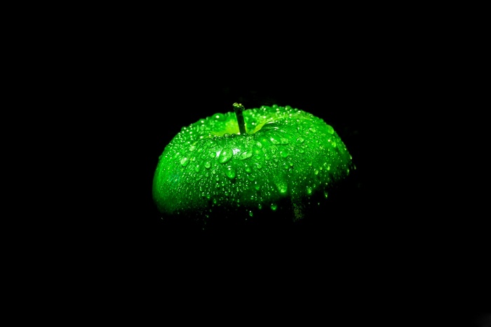 Green apple with water droplets on black background