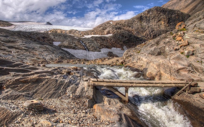 Wooden bridge over a mountain stream with a glacier