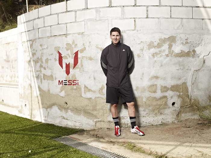 Lionel Messi standing by a wall with his logo