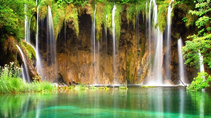 Waterfalls cascading over mossy rocks into a clear green lake