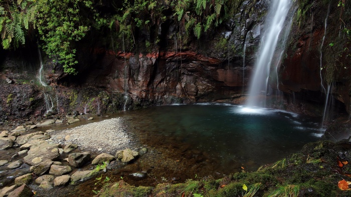 Waterfall cascading into a clear pool in a rocky grotto
