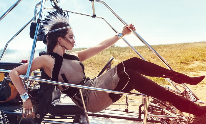 Emilia Clarke in a dune buggy wearing a headdress